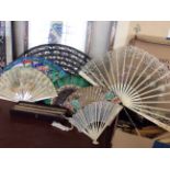 A selection of various fans, some with painted designs, some feather, some with lace trim, some