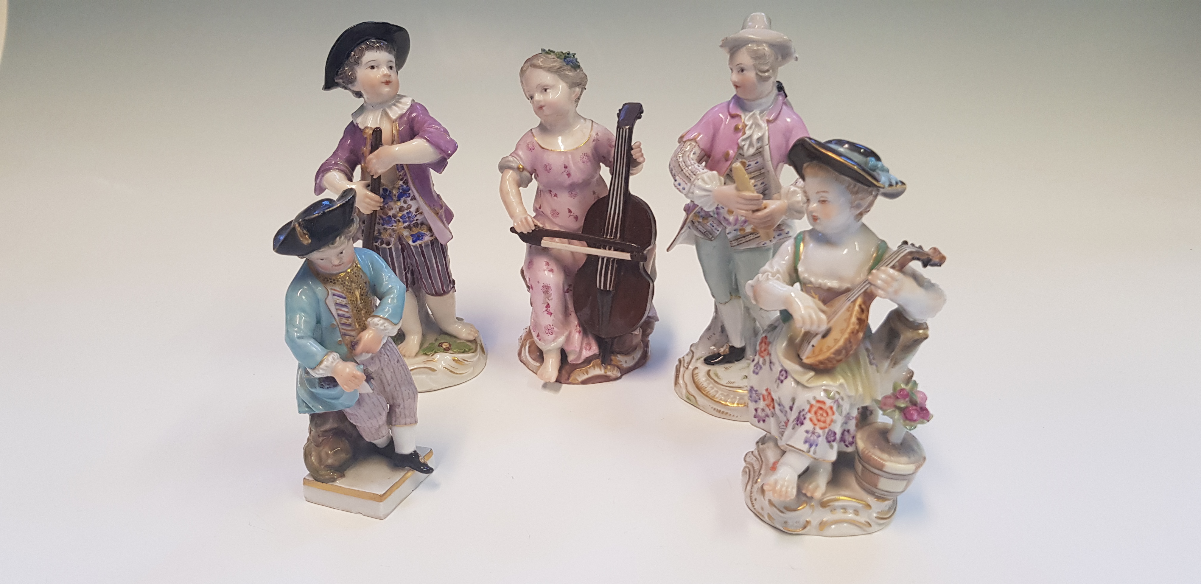 Five Meissen figurines, four with instruments, one holding grapes, painted with gold detail, all