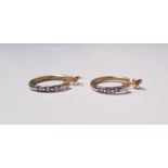 A pair of yellow gold marked 750 hoop earrings with three diamonds on each earring. On line