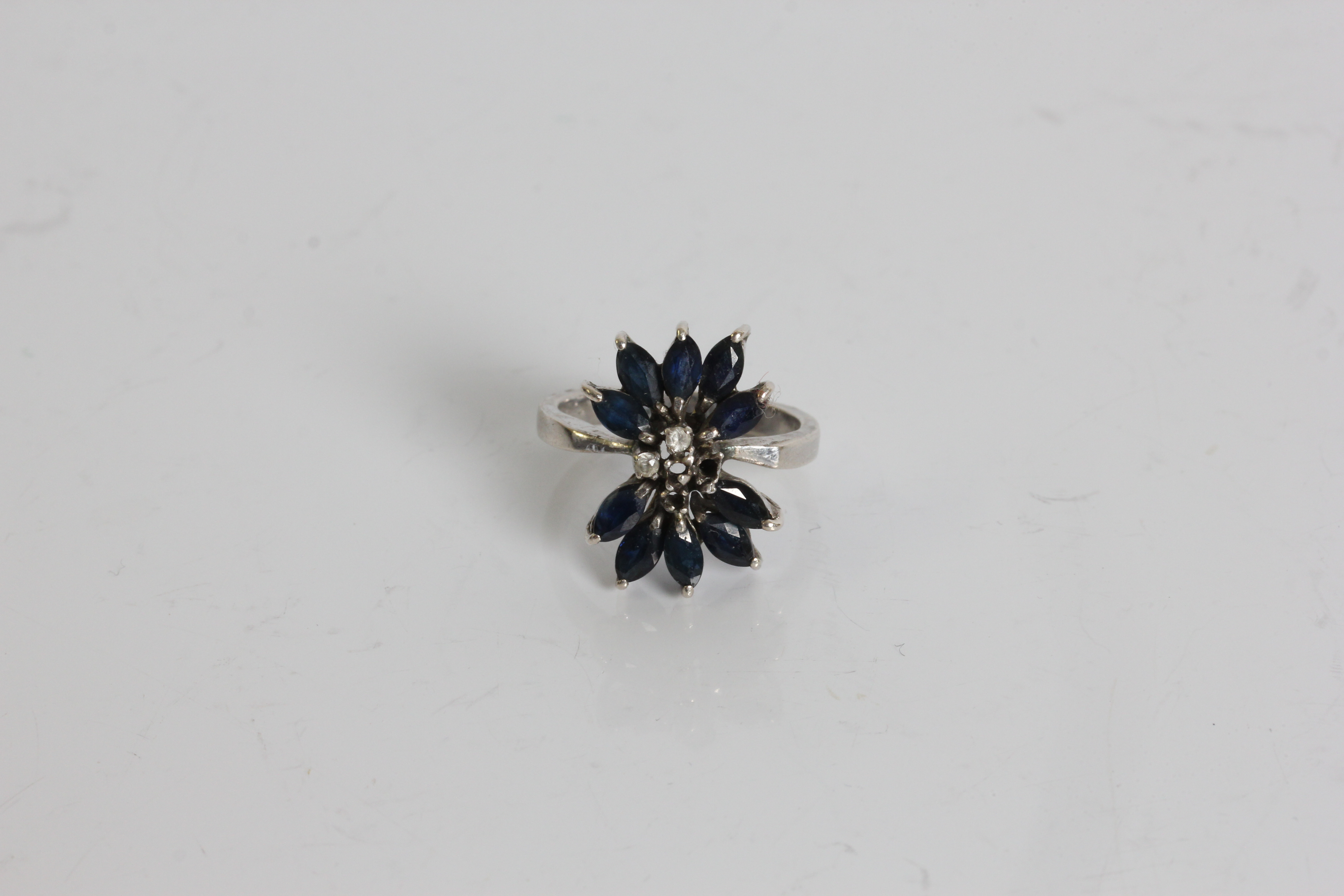 A white gold sapphire and diamond chips ring in design of a flower with petals , marked 18k, ring