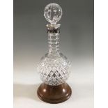 A cut glass hoggit decanter with stopper and silver collar, sitting on wooden base, height 34cm.