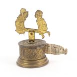 A gilt brass novelty tape measure the leaf scroll decorated cylinder base below a winder in the form