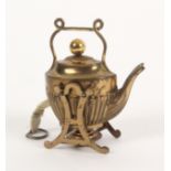 A gilt brass novelty tape measure in the form of a tea kettle on stand, the complete printed tape in