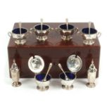 A six piece silver condiment set with six spoons contained in a fitted mahogany box, comprising four