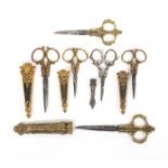 Six pairs of late 19th Century ornamental desk scissors with sheaths, comprising a graduated pair in