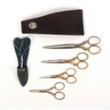 A cased set of four scissors and a scissor and thimble set, the first with oval section blades to