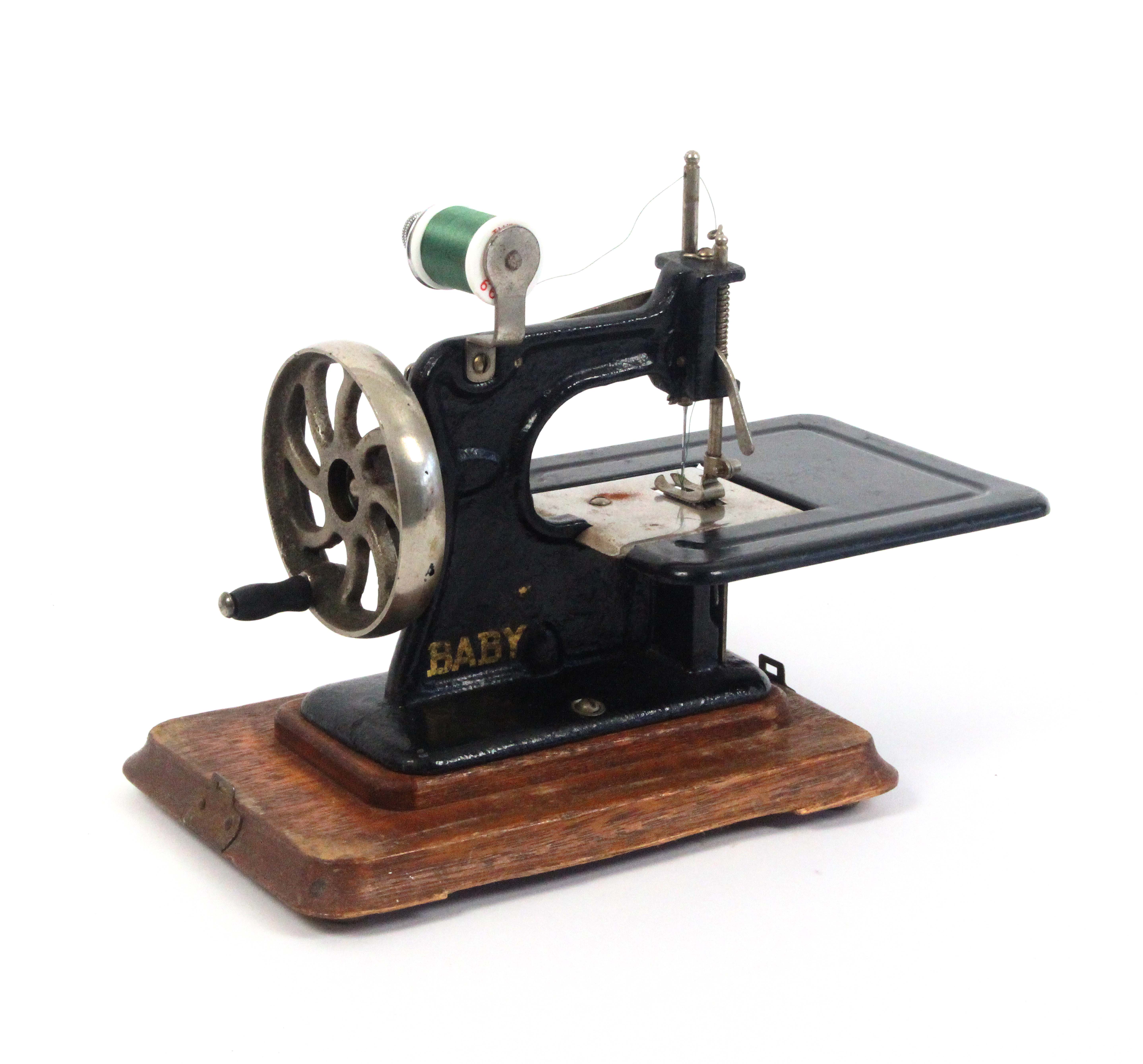 An early 20th Century sewing machine ‘Baby’, in gilt on black, wooden plinth base, additional