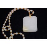 Large carved white jade pendant suspended on a bea