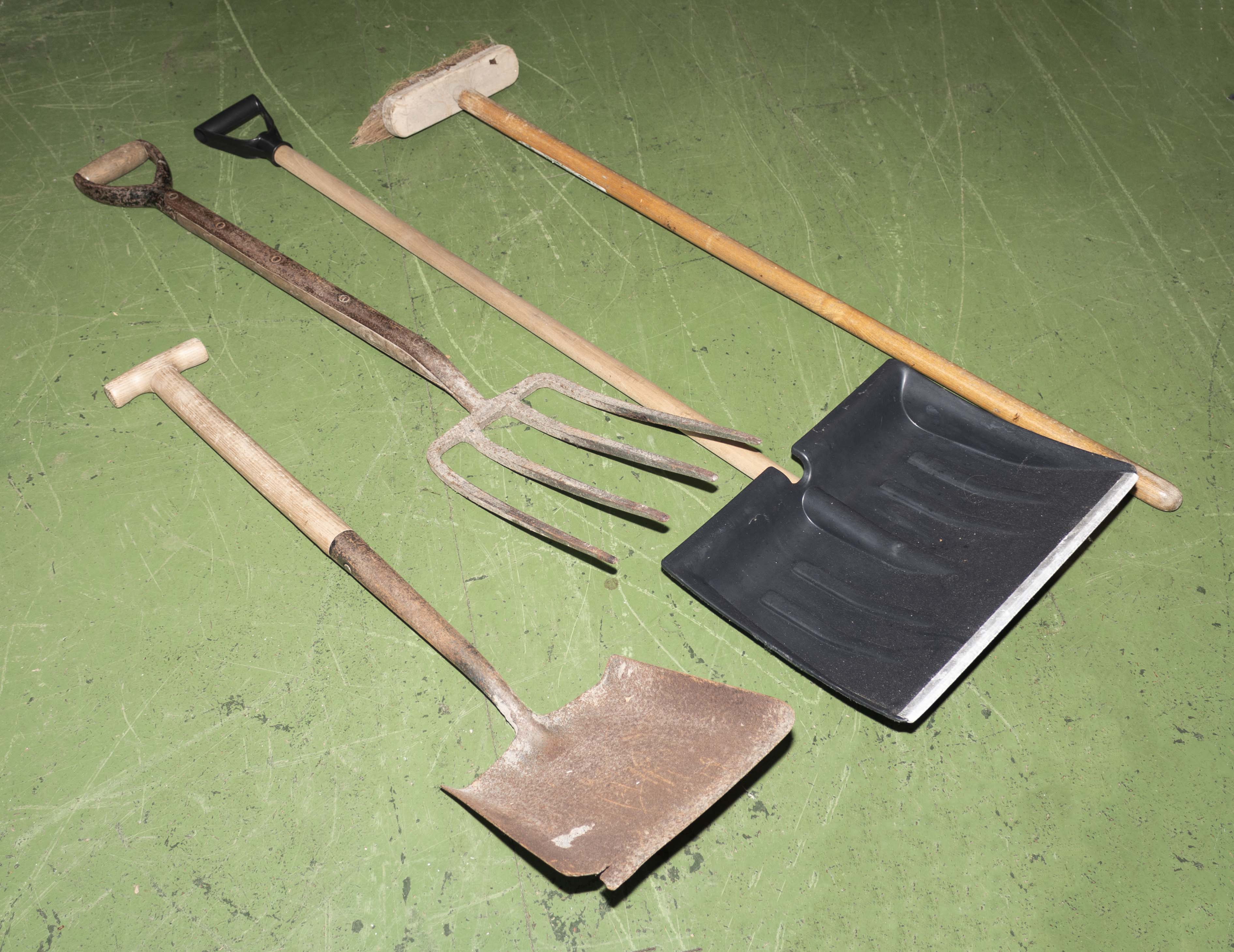 A snow shovel, brush, garden fork and shovel