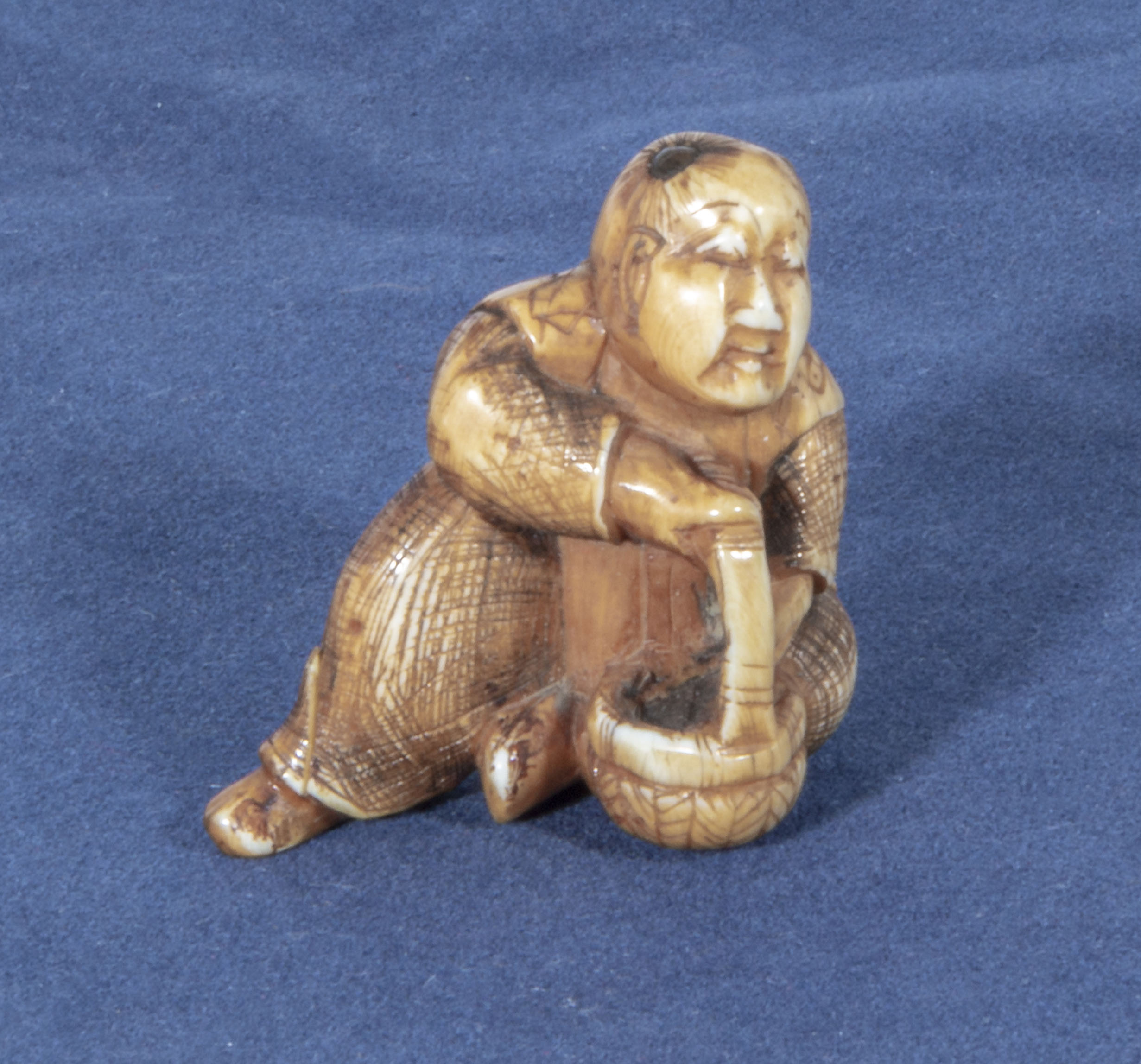An antique netsuke depicting a man with small horn roundells onlaid on his head carrying a basket,
