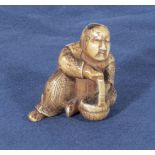 An antique netsuke depicting a man with small horn roundells onlaid on his head carrying a basket,