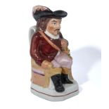 An antique Staffordshire Toby jug, in the form of a seated cavalier wearing a red coat and holding a