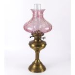 A brass oil lamp with cranberry glass shade