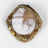 Victorian cameo carved brooch in a gold metal frame depicting a village scene with a female figure.