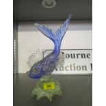 A Murano style blue glass fish with yellow eyes and silver inclusions on a shaped clear glass base