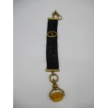 A 19th century gold coloured metal and black fabric fob with a clasp, chain, engraved ends and