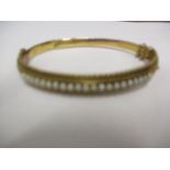 A 15ct gold bangle with safety chain and a row of seed pearls, total weight 10.75g