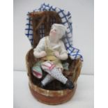 A 19th century German figure of a cobbler sitting in a barrel chair draped in a blue and white