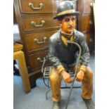 A painted composition model of Charlie Chaplin, sitting on a metal chair