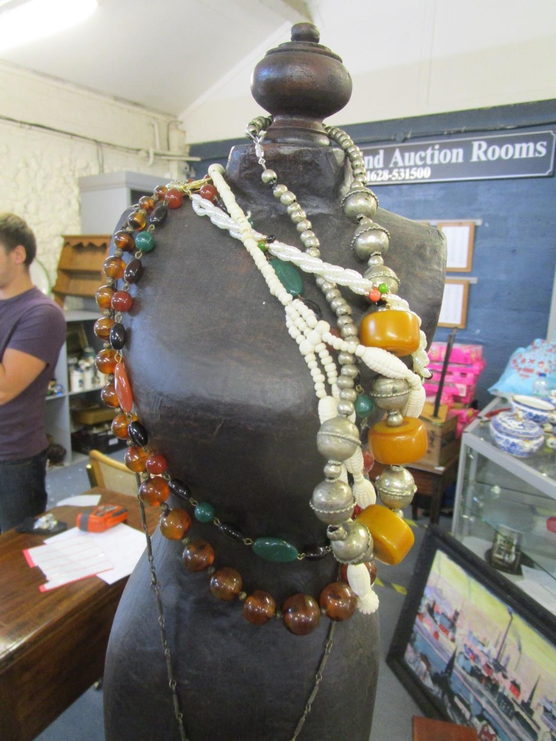 A display mannequin on wooden stand with a selection of beaded necklaces and pendants to include