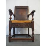 An 18th century oak Wainscote chair with a turned, carved crest, a panelled back, scrolled arms,