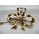 A rose coloured metal brooch in the form of a ribbon, set with three diamonds and attached with a