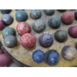 An early 20th century wooden solitaire board with sixty three stone and clay marbles