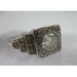 An Art Deco design white metal ring set with a central diamond on a square setting, with a diamond