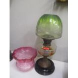 A Victorian oil lamp with a clear glass reservoir and a green and clear glass shade and a