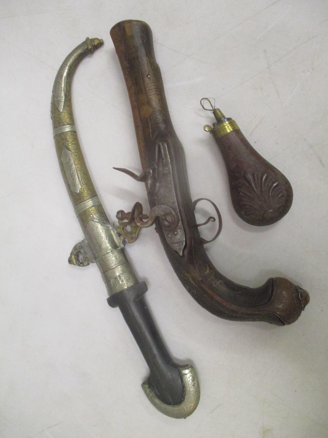 An Eastern knife with a curved blade, an inlaid flintlock pistol and a pressed metal shot flask