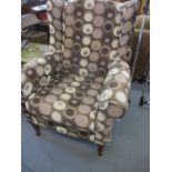 A modern wing back armchair having upholstery with shades of brown circular motifs