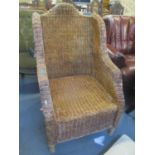 A wicker high back armchair with two loose cream cushions