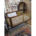 An early 20th century cane and mahogany rocking crib on stand with later bedding