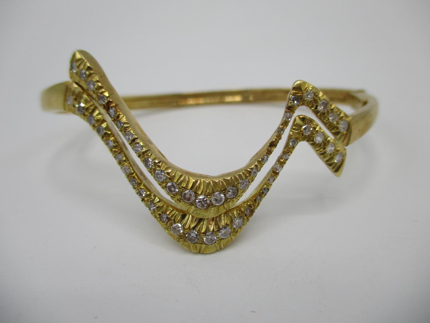 An 18ct gold coloured metal hinged bracelet of wave design set with fifty two diamonds, stamped