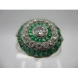 A platinum ring set with a central old cut diamond in alternating bands of emeralds and round cut