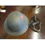 A WWII Brodie metal helmet with two stripes painted to the front and a pair of metal and leather