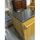 A modern light oak kitchen island with a black stone top over two short drawers, a door and a wine