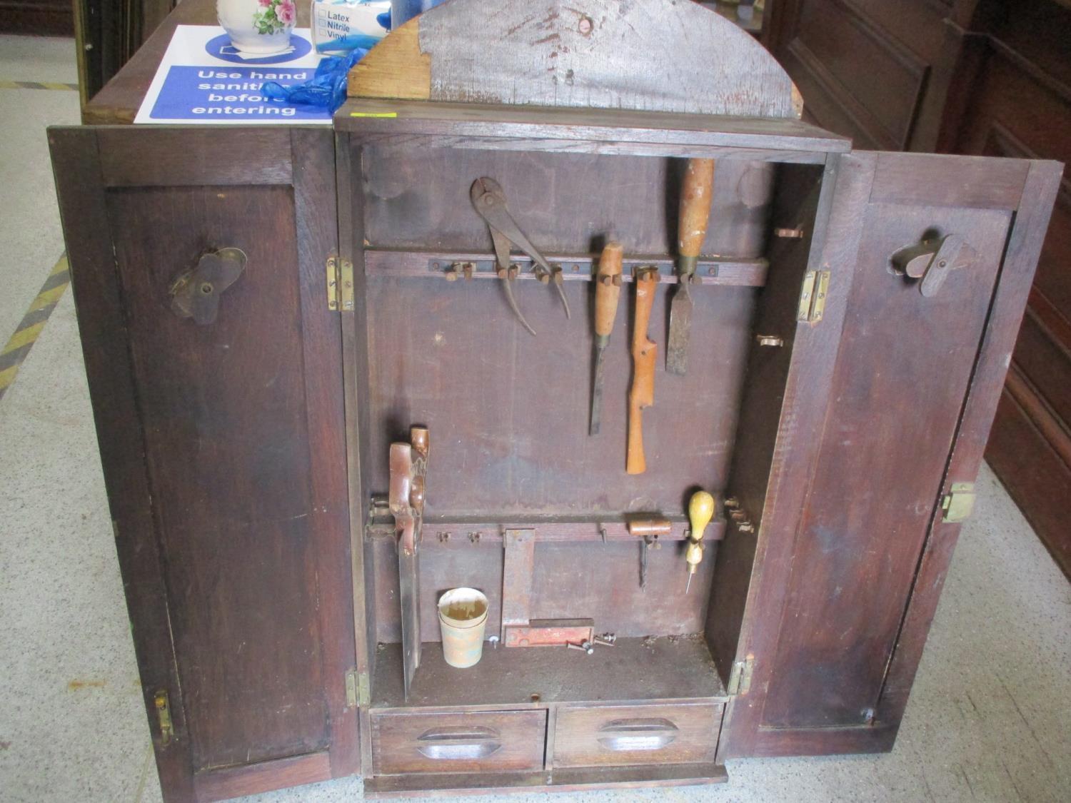 A 1930s oak finished, twin door, wall mounted tool cabinet, containing a small assortment of tools