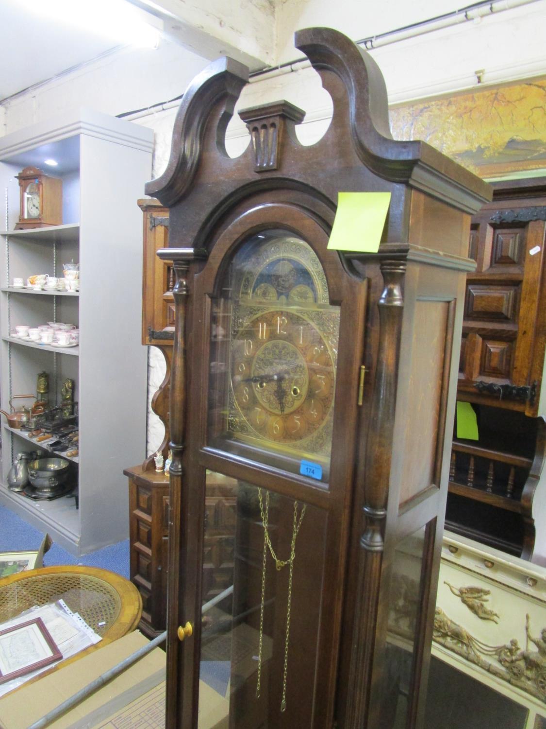 A reproduction long case clock with broken swan neck pediment, turned finial, brass arched dial,