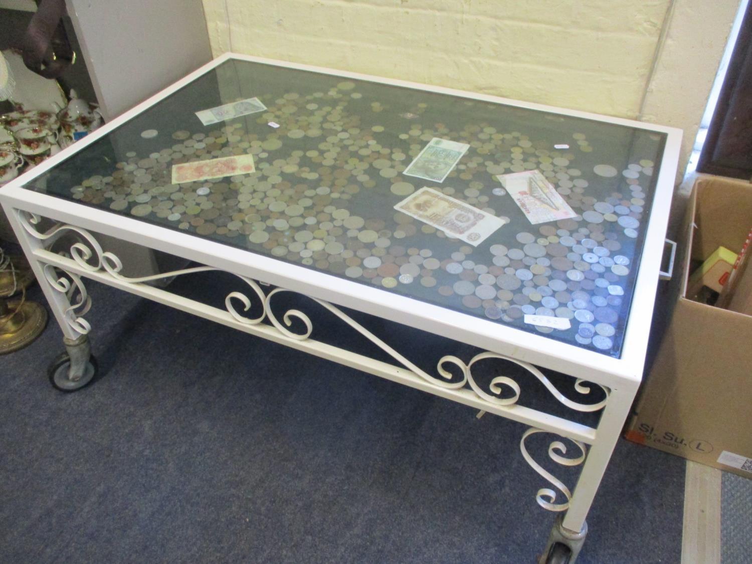 A vintage white metal and glass coffee table having a quantity of coins displayed under a glass