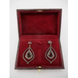 A pair of silver drop earrings set with a garnet within a band of diamonds, on a frame and garnet