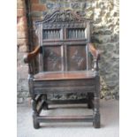A 17th/18th century oak Wainscot chair with a carved crest, panelled back, scrolled arms and planked