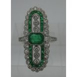 A platinum elongated ring set with a central emerald flanked by six diamonds with a band of emeralds