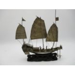 A Chinese white metal model of a junk ship, supported on a carved and pierced hardwood base