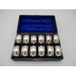 A cased set of twelve Edwardian silver napkin rings by C.T Burrows & Sons, Birmingham 1905, designed
