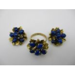 A gold ring fashioned as a flower with textured leaves, set with blue cabochons and a pair of