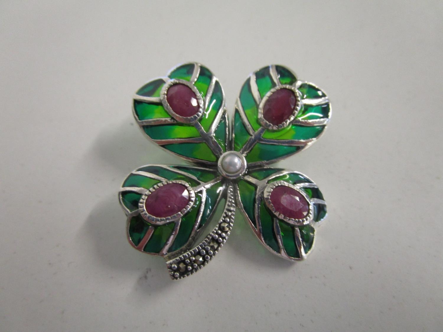 A silver and enamelled brooch fashioned as a four leaf clover, set with rubies, a pearl and