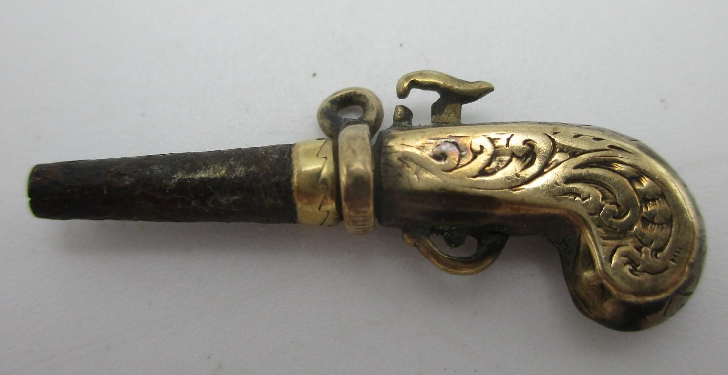 A gold coloured metal and steel watch key fashioned as a pistol with a ratchet mechanism Location: