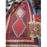 An Iranian hand woven rug in red, blue, green, white and black colours with tasselled ends, 300 x150