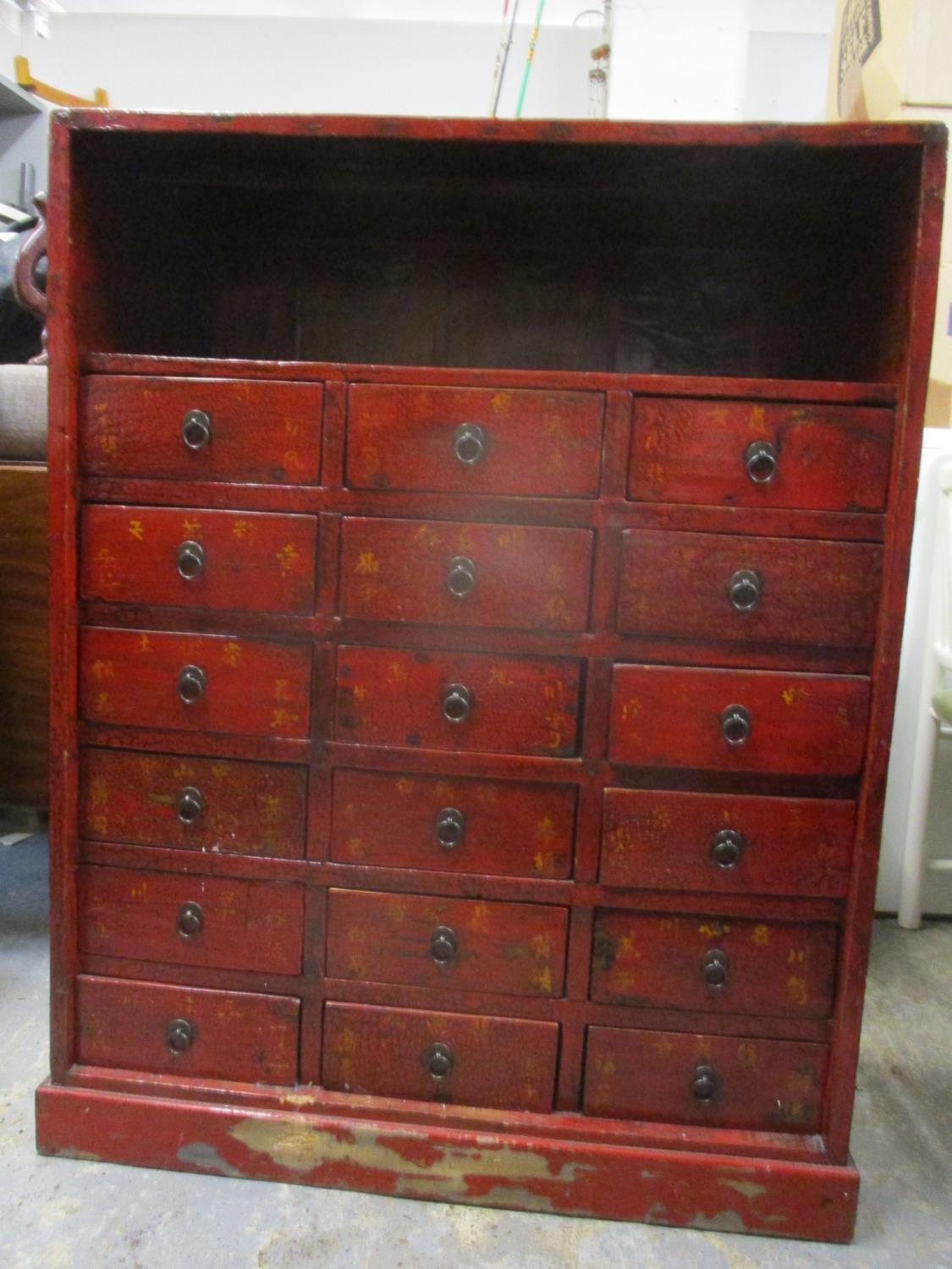 A Chinese lacquered and painted chest with a shelf over eighteen drawers on a plinth